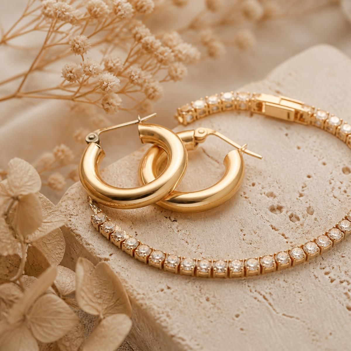 Gold hoop earrings and a diamond tennis bracelet on stone